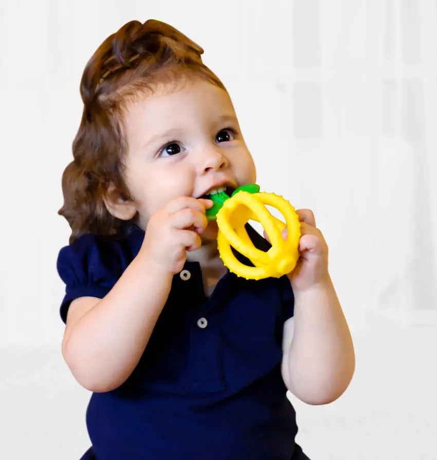 Child using the bristles of the leaves of a yellow Bitzy Biter™ Teething Ball & Training Toothbrush 