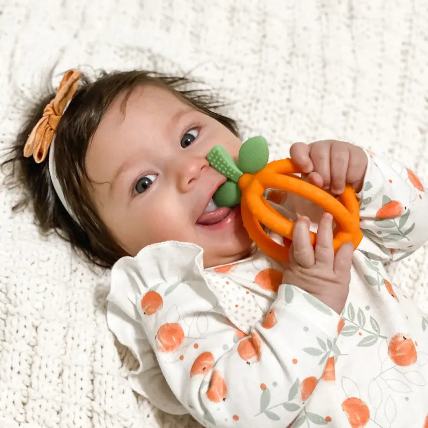 Child chewing on the green leaves of an orange Bitzy Biter™ Teething Ball & Training Toothbrush
