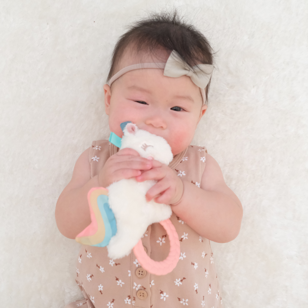 Infant chewing on unicorn Ritzy Rattle Pal™ | Plush Rattle with Silicone Teething Ring