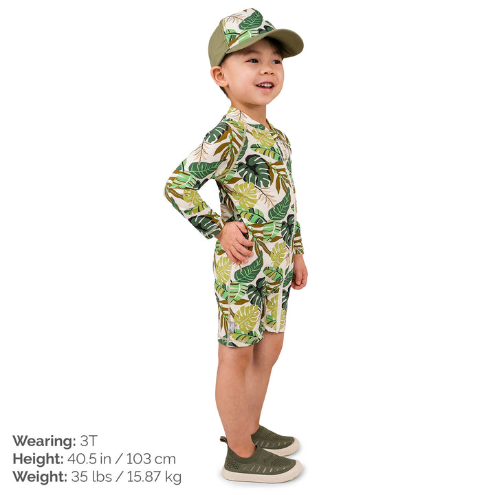 Child wearing Jan & Jul UV Jumpsuit | Green Tropical. The child is a size 3T and weighs 35lbs and is 40.5 inchs. The child is wearingcoordianting Green torpical accessories and has his hand on his hip facing us.