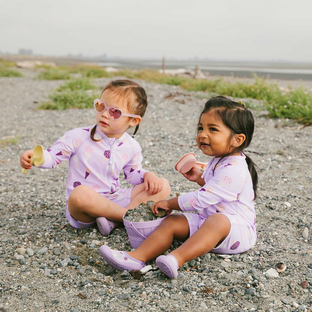 Lifestyle photo of two children on the beach wearing the Jan & Jul UV Jumpsuit | Lavendar Ice Cream