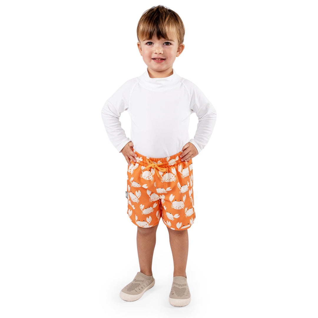 Front View of Child wearing Jan & Jul UV Swim Shorts | Crabby Crab. The child is a size 3T at 35lbs and 39.3 tall. Child is also wearing a white rash guard, and Jan and Jul Explore Shoes in a beige colour. 