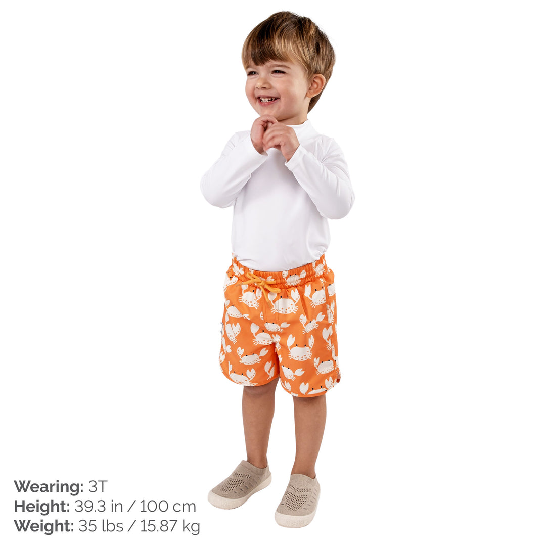 Child wearing Jan & Jul UV Swim Shorts | Crabby Crab. The child is a size 3T at 35lbs and 39.3 tall. Child is also wearing a white rash guard, and Jan and Jul Explore Shoes in a beige colour. 