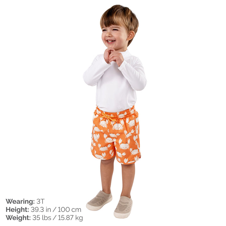 Child wearing Jan & Jul UV Swim Shorts | Crabby Crab. The child is a size 3T at 35lbs and 39.3 tall. Child is also wearing a white rash guard, and Jan and Jul Explore Shoes in a beige colour. 