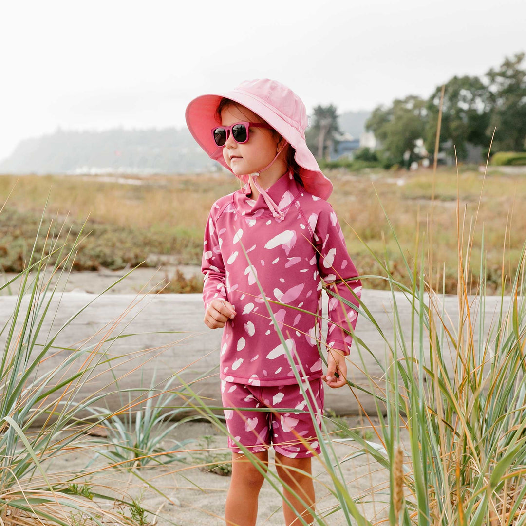 Young girl wearing Jan & Jul 2 piece swim suit with adventure hat and sugnlasses at the beach