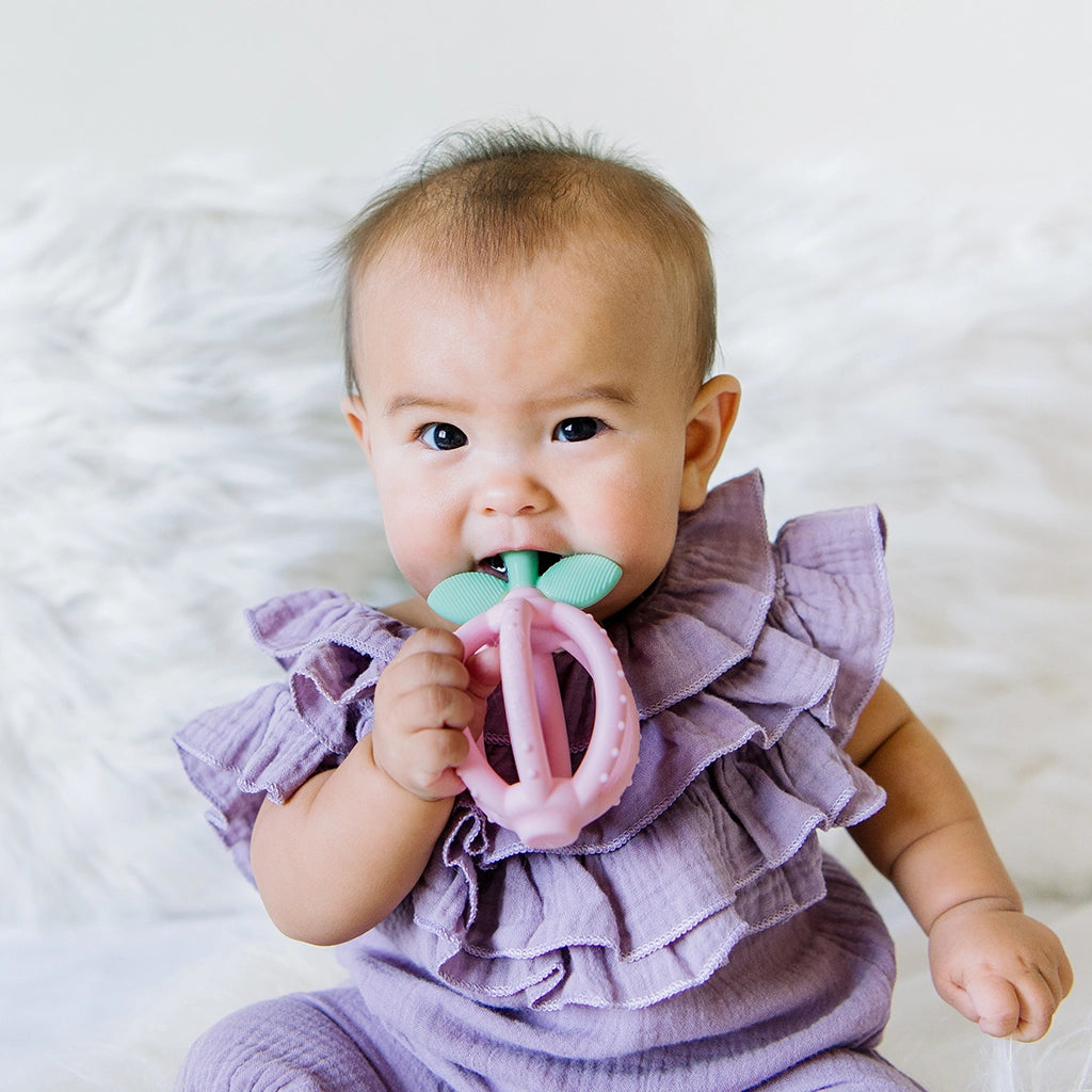 Child chewing on the stem of a pink Bitzy Biter™ Teething Ball & Training Toothbrush