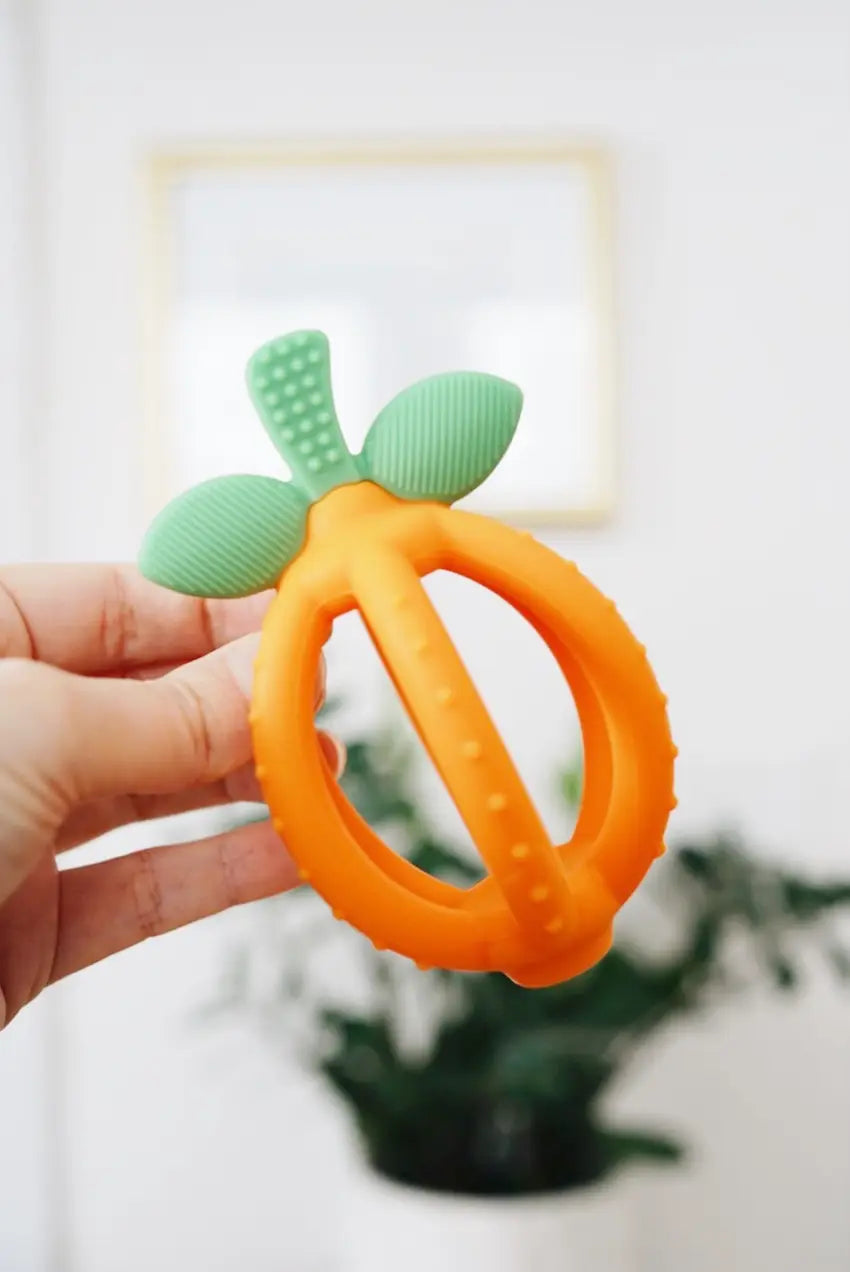 Woman's hand holding an orange Bitzy Biter™ Teething Ball & Training Toothbrush