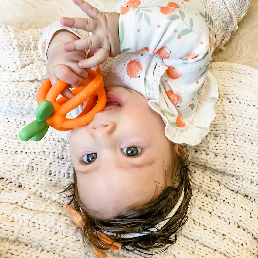 Child grasping and chewing on an Orange Bitzy Biter™ Teething Ball & Training Toothbrush
