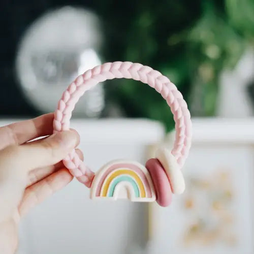 Itzy Ritzy Rattle in Pink Rainbow held by a hand. 